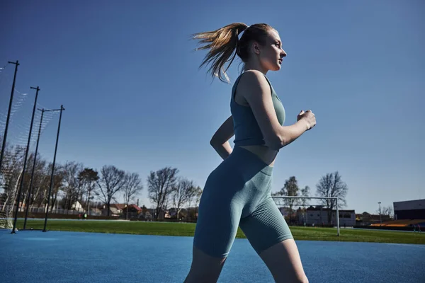 Side view of blonde fit woman in cycling shorts and crop top running outdoors, motivation and sport — Stock Photo