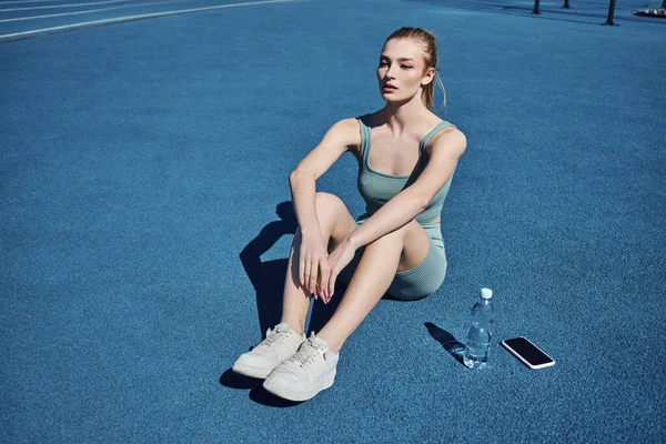 Молода спортсменка в активному одязі, сидячи поруч з пляшкою води і мобільного телефону після тренування — стокове фото