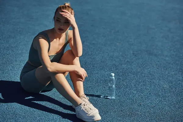 Bela esportista em activewear sentado ao lado de garrafa de água, tendo descanso após o treino — Fotografia de Stock