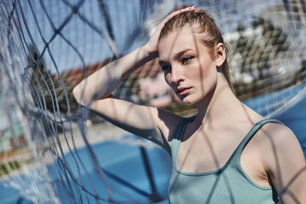 Portrait of blonde and fit woman standing in activewear near net after working out outdoors — Stock Photo
