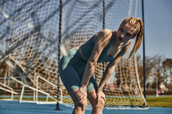Спортивная молодая женщина с хвостиком в спортивной одежде отдыхает во время тренировки на открытом воздухе возле сети — стоковое фото
