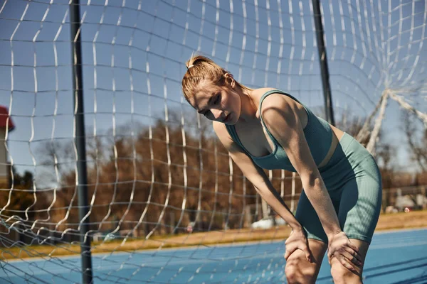 Tired young woman with ponytail in activewear resting while working out outdoors near net — Stock Photo