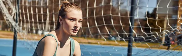 Tired young woman with ponytail in activewear resting while working out outdoors near net, banner — Stock Photo