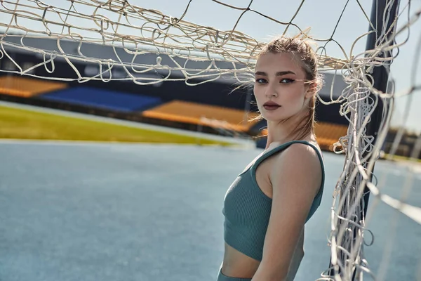 Blonde sportswoman with ponytail standing near net after workout in stadium, urban fitness — Stock Photo