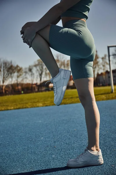 Vista parcial de la deportista flexible ejercitándose en ropa deportiva apretada al aire libre, pierna estirada - foto de stock