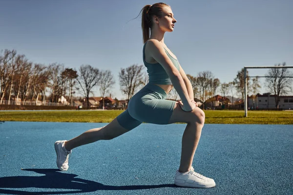 Side view of pretty young sportswoman with ponytail exercising in activewear outdoors, doing lunges — Stock Photo