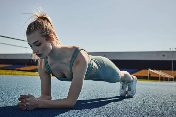 Привлекательная спортсменка с хвостиком, тренирующаяся в активной одежде возле сети на открытом воздухе, делающая доску — стоковое фото
