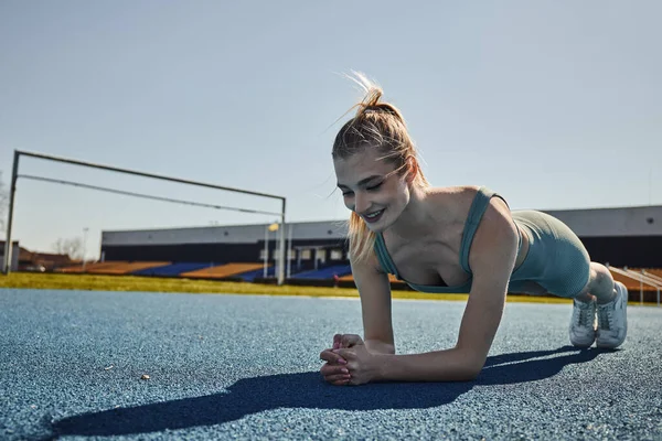 Happy sportswoman with ponytail exercising in activewear near net outdoors, doing plank — Stock Photo