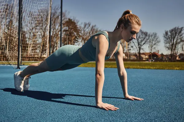 Молодая спортсменка с хвостиком, тренирующаяся в активной одежде возле сети на открытом воздухе, делающая отжимания — стоковое фото
