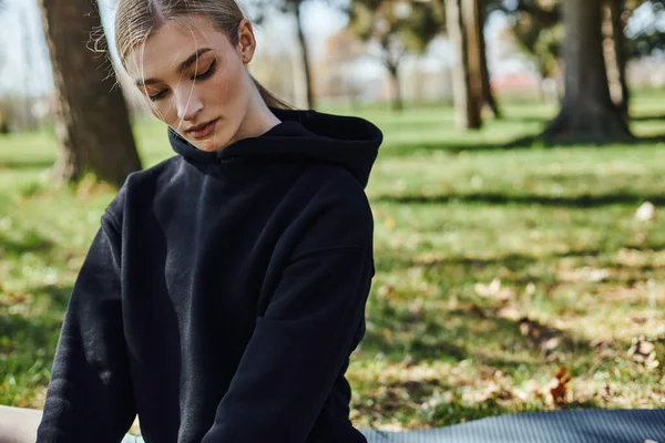 Porträt einer sportlichen jungen Frau in schwarzem Kapuzenpulli, die im grünen Park Sport treibt — Stockfoto