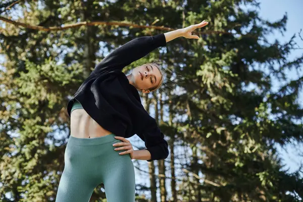 In forma giovane donna con i capelli biondi e abbigliamento sportivo che estende il suo corpo mentre si allena nel parco — Foto stock