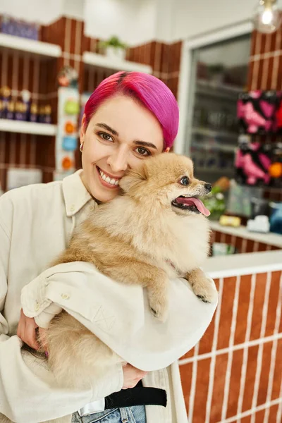 Glückliche Frau mit lila Haaren umarmt pelzigen Freund und blickt in die Kamera in einladendem Hundehotel — Stockfoto