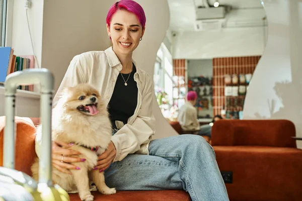 Zufriedene Frau sitzt neben Reisetasche im Haustierhotel und kuschelt lustigen Hund, Haustier-Unterkunft — Stockfoto