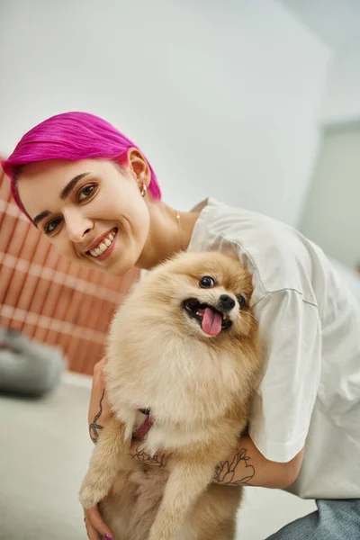 Delighted pet hotel worker embracing fluffy pomeranian spitz and smiling at camera, bonding and care — Stock Photo