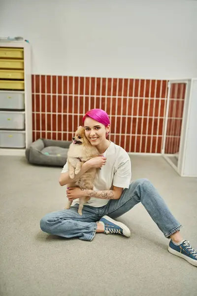 Довольная няня-собака обнимает милую померанскую шпиц и смотрит в камеру на полу в зооотеле — стоковое фото