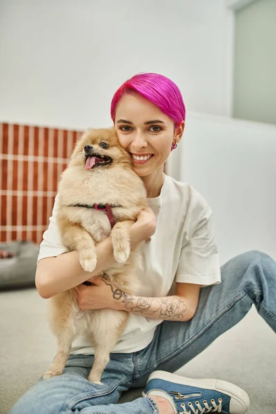 Purple-haired woman sitting on floor and embracing pomeranian spitz, affection of dog and pet sitter — Stock Photo