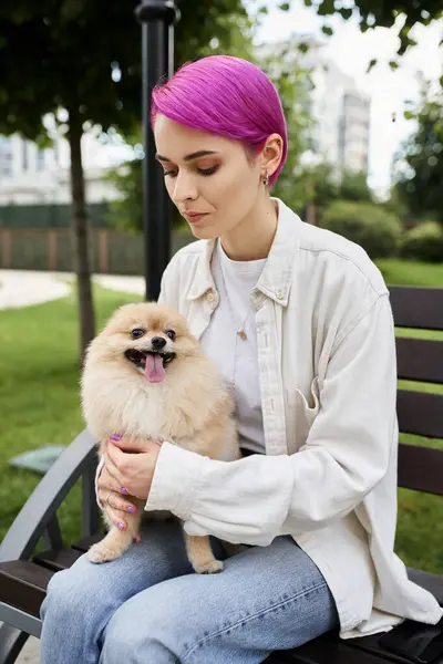 Stylish purple-haired woman embracing loveable pomeranian spitz while sitting on bench in park — Stock Photo
