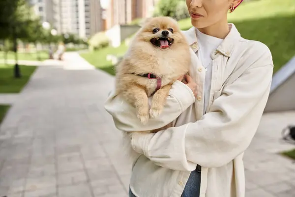 Cropped view of woman with pampered pomeranian spitz in hands walking on urban street, joyful moment — Stock Photo