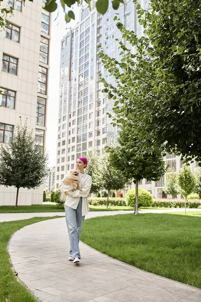 Volle Länge der stilvollen Frau mit kleinem reinrassigen Hund in den Händen, der auf der Straße spaziert, Stadtleben — Stockfoto