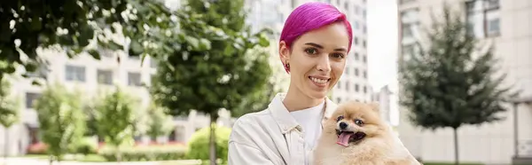 Trendy purple-haired woman with pomeranian spitz in hands smiling at camera on urban street, banner — Stock Photo
