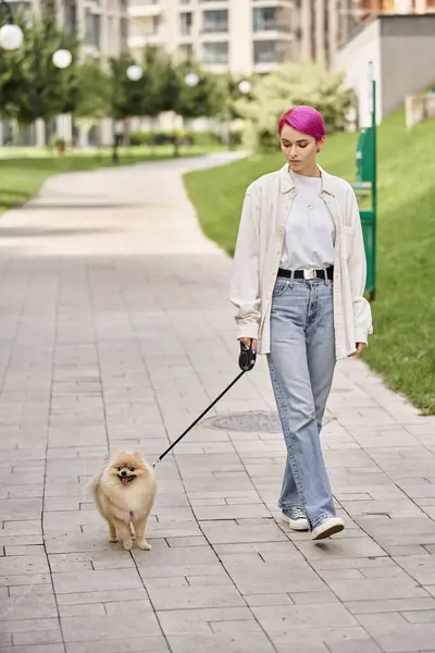Full length of trendy purple-haired woman walking with pomeranian spitz on roulette leash in city — Stock Photo