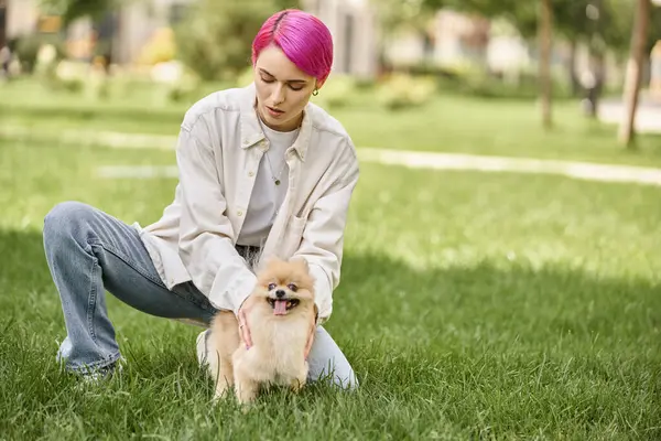Stylish purple-haired woman with adorable pomeranian spitz on green lawn in park, outdoor activity — Stock Photo