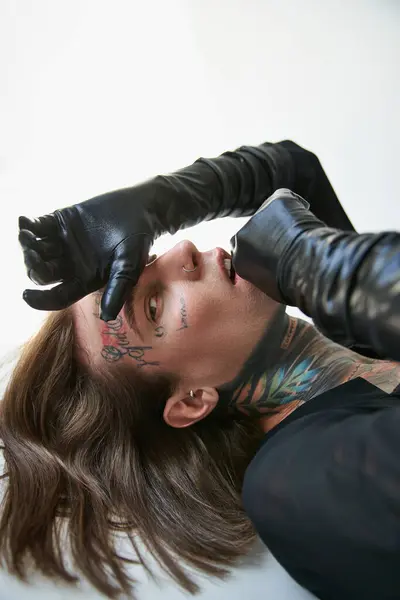 Close up of young man with tattoos and piercing posing in profile lying on floor, fashion concept — Stock Photo