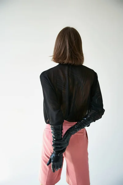 Back view of young long haired man in stylish leather gloves and pink trendy pants, fashion concept — Stock Photo