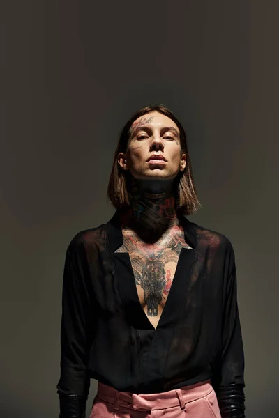 Hombre elegante guapo con tatuajes y piercing de pie quieto y mirando a la cámara, concepto de moda - foto de stock