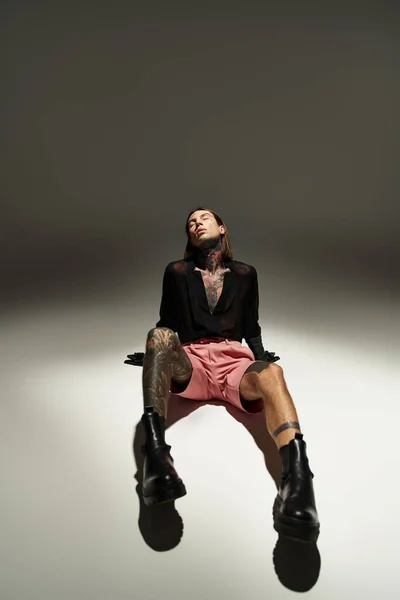Tiro vertical de modelo masculino elegante em roupa sedutora sentado no chão com os olhos fechados, moda — Fotografia de Stock