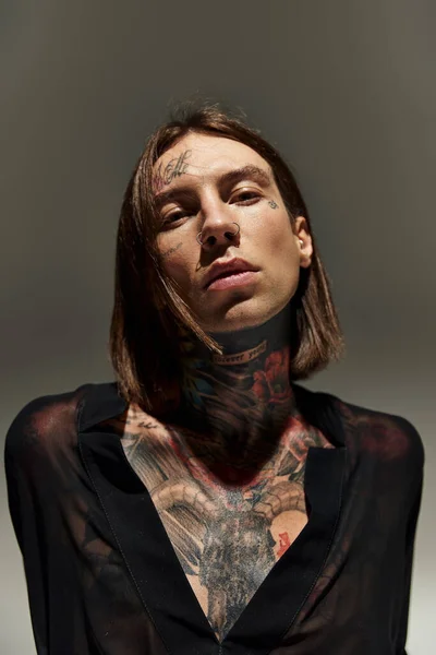 Гарний молодий чоловік в чорній блузці з татуюваннями та пірсингом дивиться на камеру, мода — Stock Photo