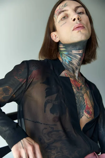 Vertical shot of handsome young man with tattoos and piercing in black transparent blouse, fashion — Stock Photo