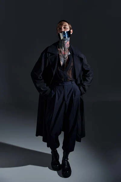 Tiro vertical de jovem em máscara futurista atado e em roupa elegante preto, olhando para a câmera — Fotografia de Stock