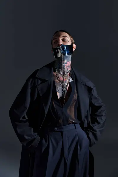 Hombre guapo con tatuajes en la máscara elegante atada posando sobre el telón de fondo negro, concepto de moda - foto de stock