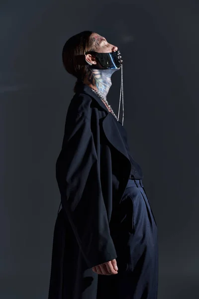 Guapo sexy hombre en negro atado máscara y elegante atuendo doblando su cuerpo ligeramente y mirando hacia arriba - foto de stock