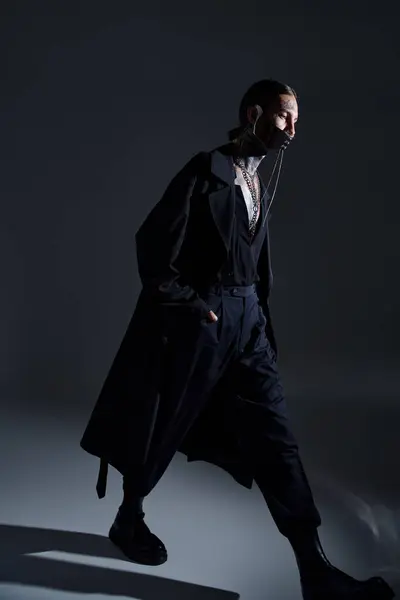 Tiro vertical de hombre con estilo en traje futurista negro con accesorios caminando y mirando hacia otro lado - foto de stock
