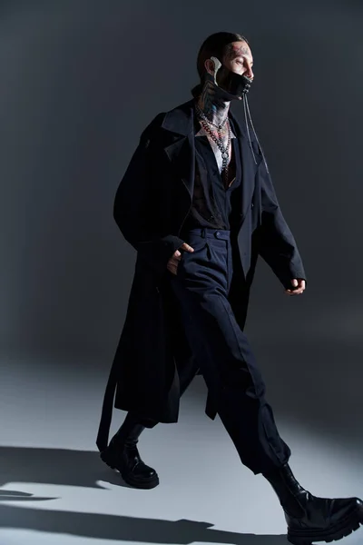 Jovem homem sexy em traje preto futurista e máscara atada andando com a mão no bolso, moda — Fotografia de Stock