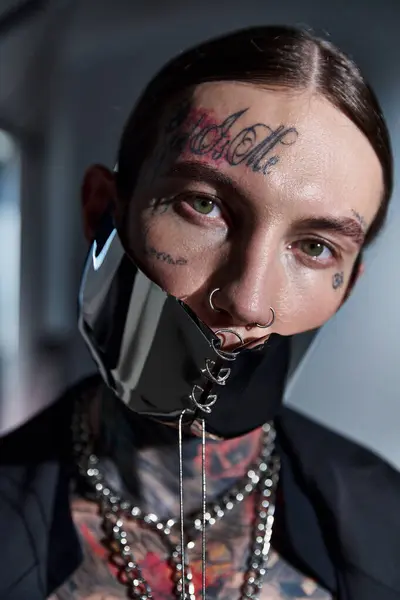 Porträt eines jungen, stylischen Mannes mit Tätowierungen in futuristischer Maske, der in die Kamera blickt, Modekonzept — Stockfoto