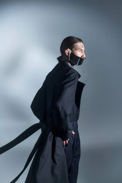 Beau jeune modèle masculin en costume élégant noir avec masque laqué posant avec les mains dans les poches — Photo de stock