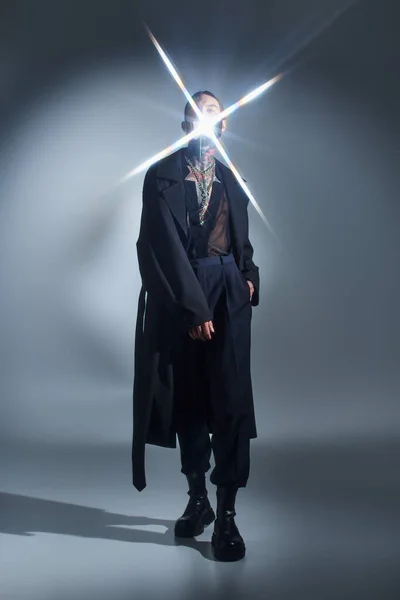 Joven en traje futurista negro posando con chispa de luz en su cara, concepto de moda - foto de stock