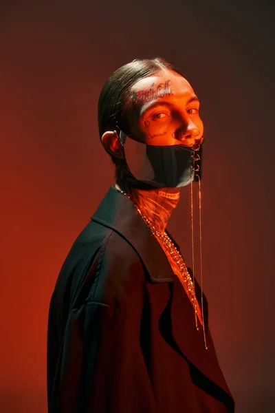 Retrato de hombre atractivo con estilo con tatuajes y máscara atada futurista mirando a la cámara, la moda - foto de stock