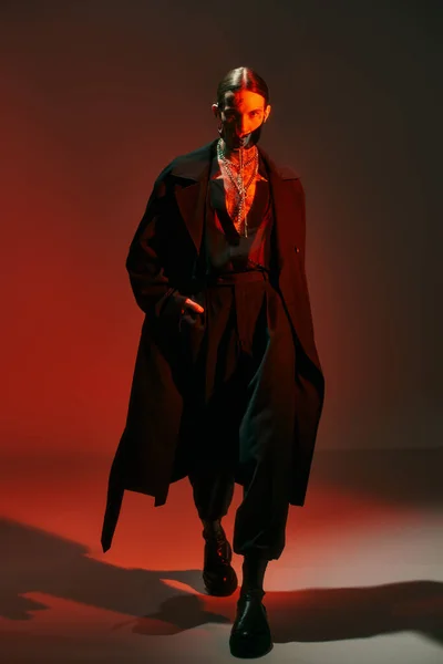 Joven sexy hombre en traje futurista con la máscara atada caminando hacia la cámara con la mano en el bolsillo - foto de stock