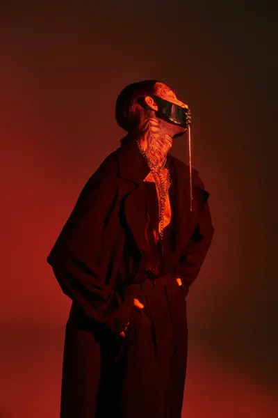 Vertical shot of sexy young man with tattoos and laced mask with hands in pockets, fashion concept — Stock Photo