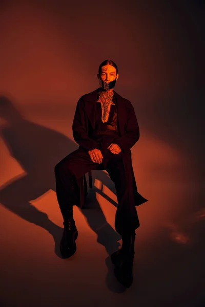 Plan vertical de l'homme sexy élégant dans un masque futuriste en regardant la caméra entourée de lumière orange — Photo de stock
