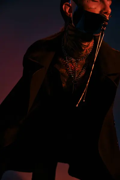 Вертикальный снимок молодого стильного мужчины с татуировками на лице в футуристической маске в окружении тёмного света — стоковое фото
