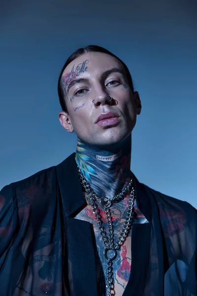 Tiro vertical de hombre joven con estilo con tatuajes y piercing mirando a la cámara, concepto de moda - foto de stock
