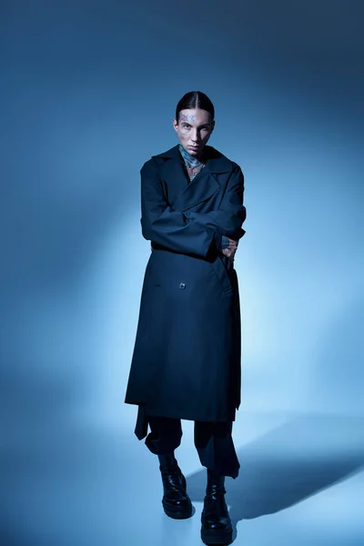 Scatto verticale di giovane uomo elegante con tatuaggi in elegante cappotto nero guardando fotocamera, moda — Foto stock
