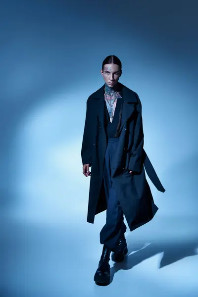 Вертикальный снимок молодой стильной мужской модели с татуировками в черном модном пальто, смотрящей в камеру — стоковое фото