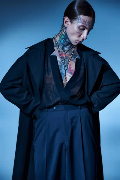 Tiro vertical de jovem homem elegante em traje preto com tatuagens posando com as mãos sobre os quadris, moda — Fotografia de Stock