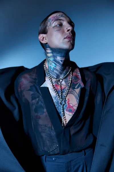 Tiro vertical de hombre atractivo de buen aspecto con tatuajes y accesorios mirando hacia otro lado, concepto de moda - foto de stock